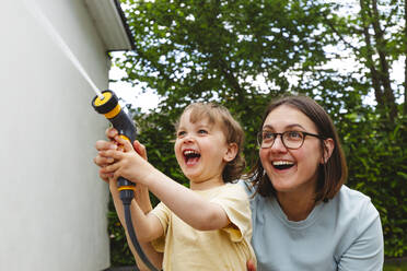 Verspielte Mutter und Sohn sprühen Wasser durch einen Gartenschlauch - IHF01049