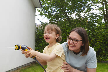 Fröhliche Mutter und Sohn spielen mit dem Gartenschlauch - IHF01050