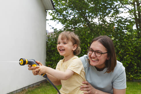 Fröhliche Mutter und Sohn spielen mit dem Gartenschlauch - IHF01050