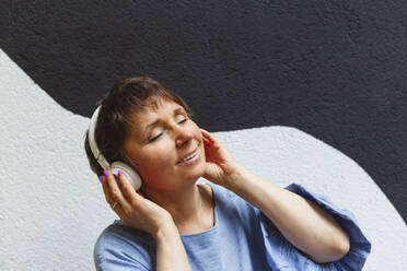 Entspannte Frau mit geschlossenen Augen, die mit Kopfhörern Musik hört - IHF01091