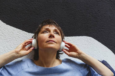 Nachdenkliche Frau, die vor einer Wand Musik hört - IHF01093