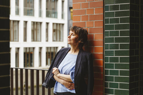 Nachdenkliche Frau mit Blazer an der Wand lehnend - IHF01097