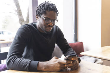 Junger Mann, der in einem Café eine Textnachricht über sein Smartphone verschickt - OSF00547