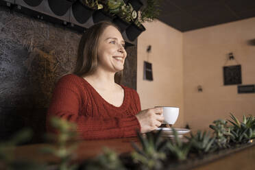 Glückliche Frau mit Kaffeetasse in einem Café sitzend - OSF00550