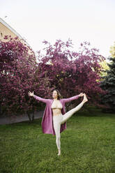 Woman standing on one leg practicing yoga in garden - EYAF01995