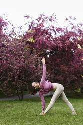 Woman practicing yoga in front of apple blossom trees - EYAF01997