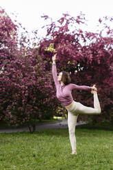 Woman with arm raised practicing yoga in apple blossom garden - EYAF01999