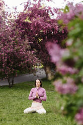 Woman with hands clasped meditating in garden - EYAF02000