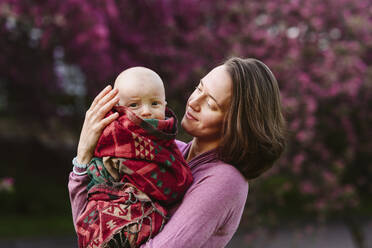 Lächelnde Mutter mit einem in eine Decke eingewickelten kleinen Jungen im Garten - EYAF02004