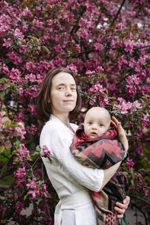 Lächelnde Frau mit kleinem Jungen vor einem Apfelblütenbaum stehend - EYAF02007