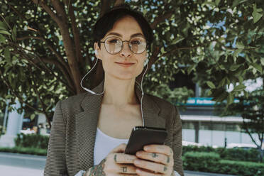 Smiling businesswoman listening music in front of tree - OIPF02294