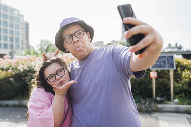 Playful Bruder und Schwester machen Gesichter und nehmen selfie durch smart phone - MEUF07330