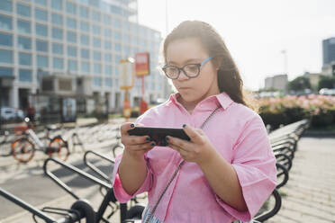 Teenager-Mädchen mit Down-Syndrom spielt Videospiel auf einem Smartphone - MEUF07354