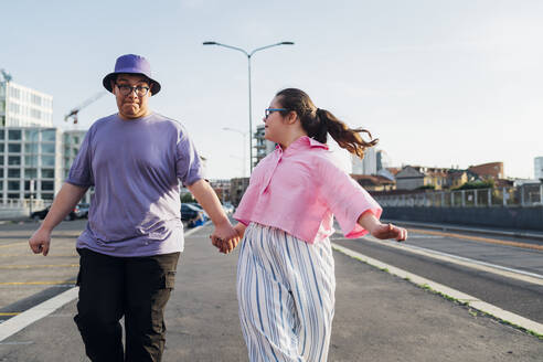 Brother and sister with down syndrome holding hands and walking on street - MEUF07398