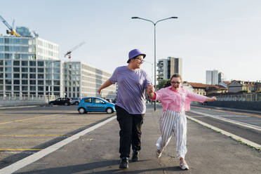 Glücklicher Bruder und Schwester mit Down-Syndrom halten sich an den Händen und laufen auf der Straße - MEUF07399