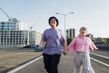 Happy brother and sister holding hands and walking on street - MEUF07400
