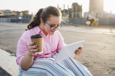 Teenage girl with disposable coffee cup using tablet PC by street - MEUF07415