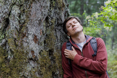 Mann mit geschlossenen Augen lehnt an einem Baum im Wald - TYF00362