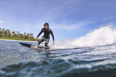 Mann mit Hut beim Surfen im Meer an einem sonnigen Tag - KNTF06771