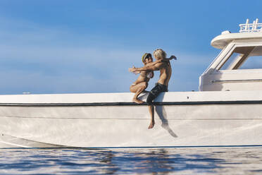 Lächelnde Frau umarmt ihren Freund auf einem Boot sitzend - KNTF06775