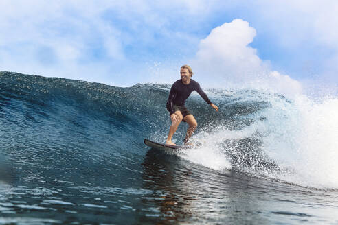Glücklicher Mann beim Surfen auf dem Meer vor einem bewölkten Himmel - KNTF06777