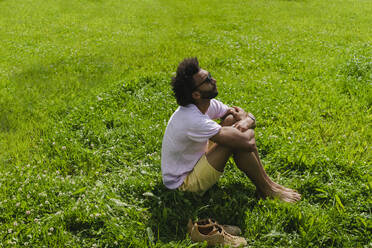 Mann umarmt Knie sitzend auf Gras im Park - SEAF01134