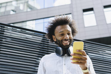 Glücklicher Mann mit Kopfhörern und Smartphone vor einem Gebäude - SEAF01148