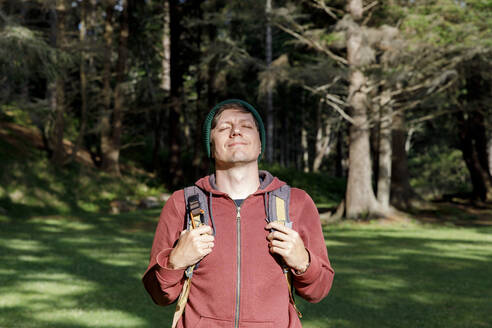 Smiling man with eyes closed standing in forest on sunny day - TYF00371