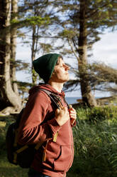 Man with backpack enjoying sunlight in forest - TYF00372