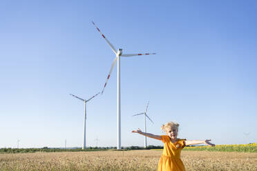Mädchen mit ausgestreckten Armen vor einer Windkraftanlage stehend - SVKF00408
