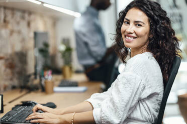 Lächelnde Geschäftsfrau bei der Arbeit am Computer im Büro - JSRF02165