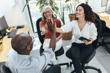 Business colleagues giving high-five to each other at office - JSRF02178