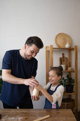 Smiling father and daughter holding dough near table at home - ADSF36093