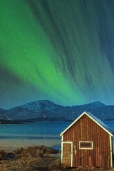 Aurora Borealis (Nordlicht) über der roten Hütte am Strand von Ramberg, Landkreis Nordland, Lofoten, Norwegen, Skandinavien, Europa - RHPLF22577