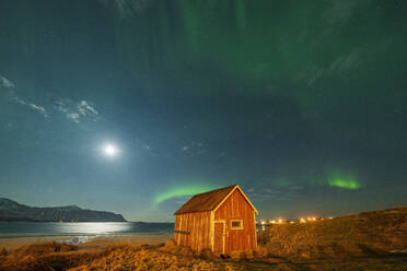 Rote Holzhütte am Sandstrand, beleuchtet vom Mond während der Aurora Borealis (Nordlicht), Ramberg, Landkreis Nordland, Lofoten, Norwegen, Skandinavien, Europa - RHPLF22578