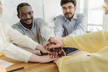 Business colleagues stacking hands at desk in office - OSF00581