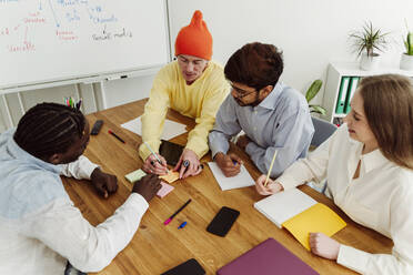 Businessman showing adhesive note to colleagues at desk in office - OSF00589