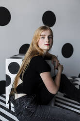 Schönes Teenager-Mädchen sitzt vor einer gepunkteten Wand - LLUF00804