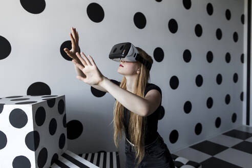 Girl gesturing wearing virtual reality headset in front of dotted wall - LLUF00806