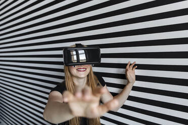 Smiling teenage girl gesturing wearing virtual reality headset - LLUF00815