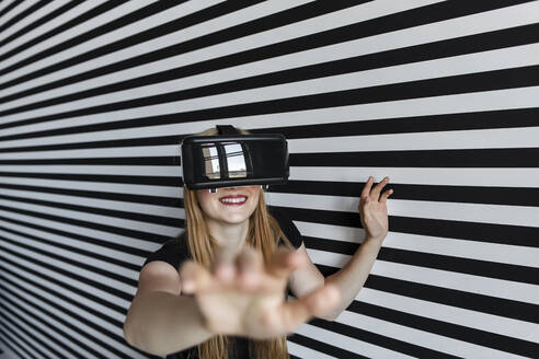 Lächelndes Teenager-Mädchen, das ein Virtual-Reality-Headset trägt und gestikuliert - LLUF00815