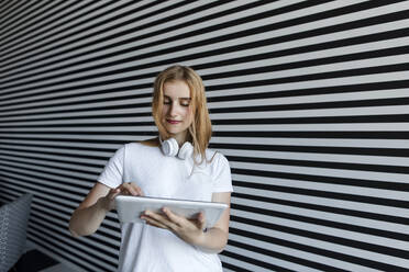 Girl with headphones using tablet PC in front of striped wall - LLUF00822