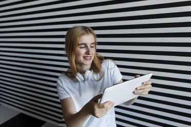Schönes Teenager-Mädchen mit Tablet-PC vor gestreifter Wand - LLUF00825