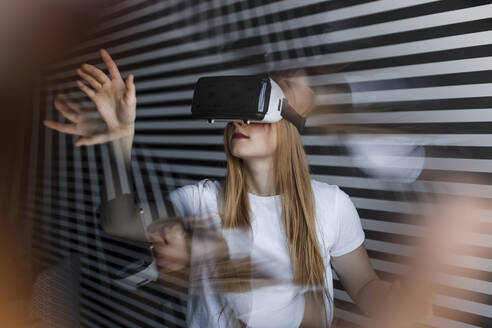 Teenager-Mädchen mit Virtual-Reality-Headset gestikuliert an einer gestreiften Wand - LLUF00830