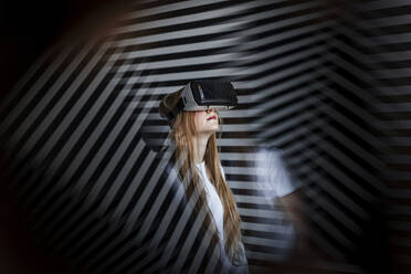 Mädchen mit blondem Haar trägt Virtual-Reality-Headset an gestreifter Wand - LLUF00832