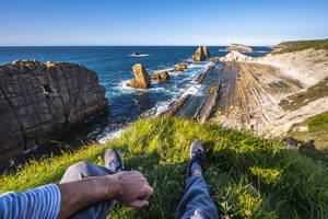Niedriger Ausschnitt eines männlichen Wanderers, der auf einer Klippe sitzt und den Blick auf das Meer und den Himmel genießt - ADSF36113