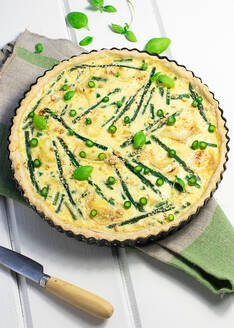 Draufsicht auf die leckere Spargel-Quiche mit Basilikumblättern auf dem Holztisch - ADSF36153