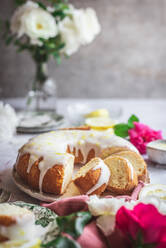 Biskuit-Zitronenkuchen auf einem Tisch neben weißen und rosa Rosen mit Blütenblättern - ADSF36181