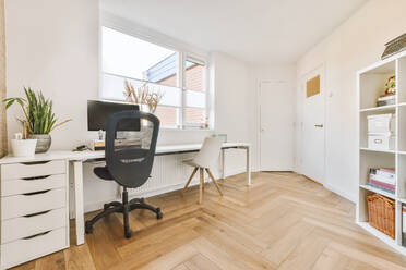 Comfortable chair placed near table with computer monitors against blank whiteboard and mirror in light home office in contemporary flat - ADSF36184