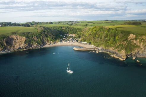 Aerial view of Yacht anchored in Polkerris harbour with view of harbour, beach and surrounding countryside, Par, Polkerris, Cornwall, United Kingdom. - AAEF15104